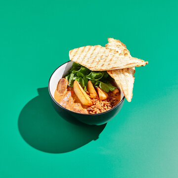Sausage chili with potatoes and crispy bread in minimalistic style. Mexican food on colour background with hard shadow. Chili con carne with sausage in contemporary concept.