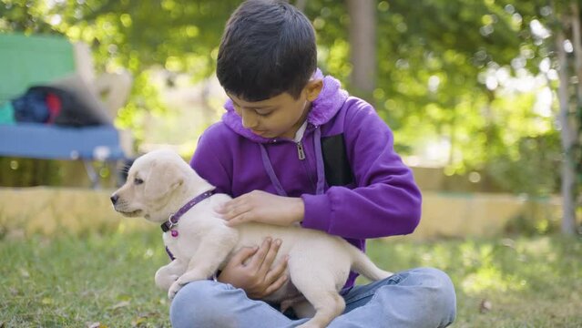 Young Indian Kid playing by holding puppy dog at park - concpet companion, friendship, childhood and recreation