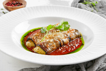 Eggplant rolls stuffed with tomato and cheese. Baked eggplant and cheese rollatini. Eggplant appetizer in white plate on stone background. Plant-based menu.