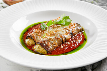 Eggplant rolls stuffed with tomato and cheese. Baked eggplant and cheese rollatini. Eggplant appetizer in white plate on stone background. Plant-based menu.