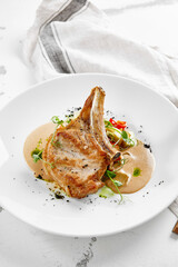 Roasted pork steak with vegetables garnish and sauce. Bone-in ribeye pork chops. Main course of pork in rustic style.