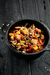 Yakisoba noodle with chicken and vegetables on wooden background. Japanese stir fry noodles in wok on black table with ingredients. Chicken with buckwheat soba on wok. Oriental cuisine. Wok menu.