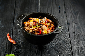 Yakisoba noodle with chicken and vegetables on wooden background. Japanese stir fry noodles in wok on black table with ingredients. Chicken with buckwheat soba on wok. Oriental cuisine. Wok menu.