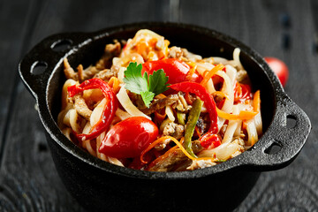 Japanese stir fryed udon noodles in wok. Udon noodle with beef and vegetables on wooden background. Asian noodles on black table with ingredients. Wok menu.
