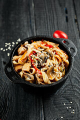 Stir fried udon noodles in wok. Udon noodle with chicken and mushrooms on wooden background. Asian...