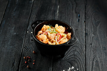 Stir fried udon noodles with shrimps in wok. Udon noodle with prawn on wooden background. Seafood udon. Asian noodles on black table with ingredients. Wok menu for japanese restaurant.