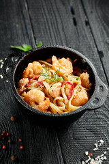 Stir fried udon noodles with shrimps in wok. Udon noodle with prawn on wooden background. Seafood udon. Asian noodles on black table with ingredients. Wok menu for japanese restaurant.