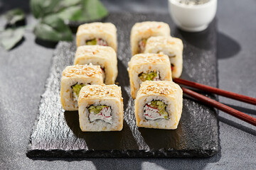 Maki sushi on dark stone table. Sushi roll crab, cheese, cucumber inside and tamago outside. Style concept japanese menu with black background, leaves and hard shadow.
