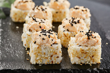 Maki sushi on dark stone table. Sushi roll in seasame and crab topped. Style concept japanesse menu with black background, leaves and hard shadow.