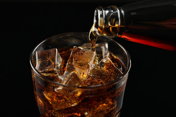 Pouring refreshing soda water from bottle into glass on black background, closeup