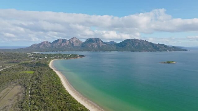 4k high angle aerial drone footage and flight over Muirs Beach with Coles Bay and the famous Hazards mountain range in the background, part of Freycinet Peninsula National Park, Tasmania, Australia.