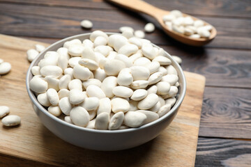 Raw white beans and bowl on wooden table, closeup