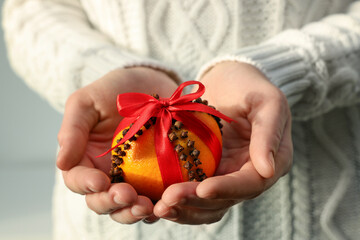 Woman holding pomander ball with red ribbon made of fresh tangerine and cloves on light background, closeup