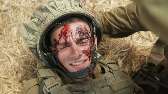 Severely wounded soldier with multiple large blood wounds to his face shakes his head while talking to his colleague. Close up shot
