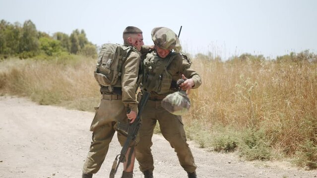 Heavily wounded soldier with bleeding right leg is helped up by his colleague and gets his helmet on. Close up shot