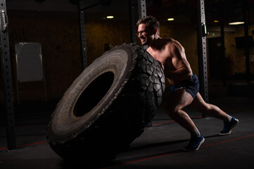 Fototapeta na wymiar Caucasian man pushing a car tire in the gym. 