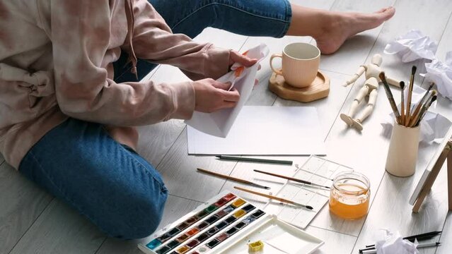 Unrecognizable woman sitting on floor at home and crumple paper because drawing is bad. Home tutoring, education, hobby or leisure concept. 