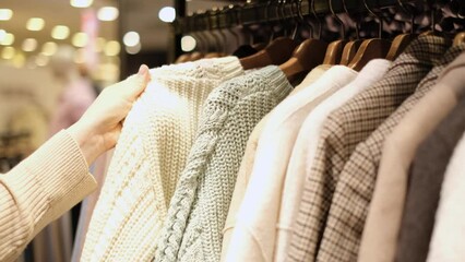 Girl chooses knitted clothes hanging on hanger in a store close-up.