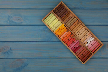 Drawing pastel set in box on light blue wooden background, top view. Space for text