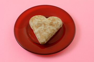 Soft heart shaped ginger cookie on red glass plate on pink background
