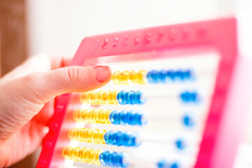 Child's hand holding yellow and blue bead abacus with pink frame.