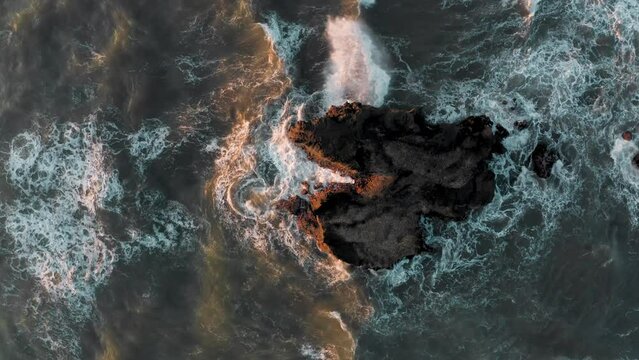 Amazing tidal waves with white water splashing on rock small island popping out of sea in golden orange sunlight at golden hour. Bali island sunset aerial copter scene with ocean shore and surf. 