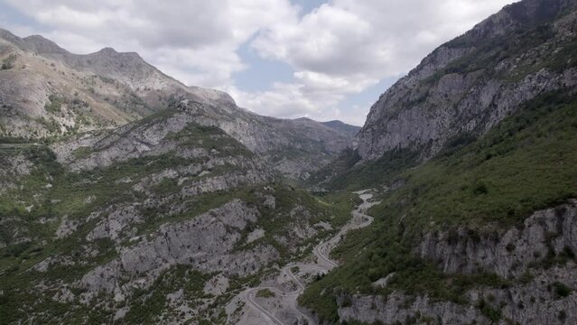 Drone video of frontal plane advancing on the Sh20 highway in Albania, at the height of Javor and Mreg, snake road, small houses of the town can be seen, cloudy sky