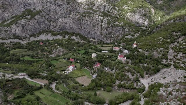 Descriptive panning Drone video advancing on the Sh20 highway in Albania, over a village in a valley at the height of Javor and Mreg, cloudy sky, houses in the village and farmland.