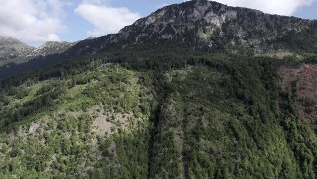 Video with Drone of front plane crane descending to a mountain of the Vermosh valley, the sh20, Albania. Clear sky with some clouds and greenish mountains with trees and vegetation.