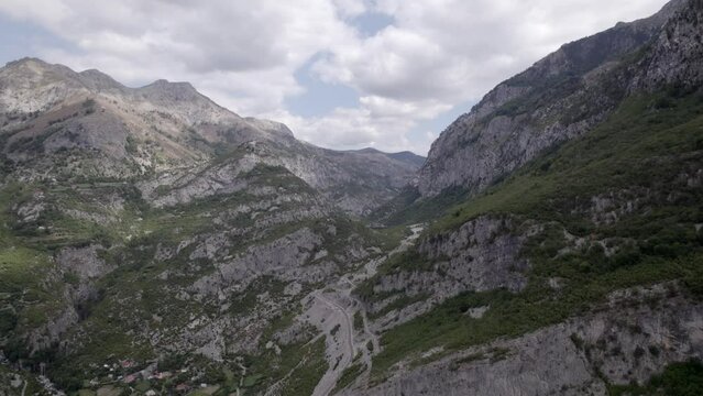 Drone video of frontal plane advancing on the Sh20 highway in Albania, at the height of Javor and Mreg, snake road, small houses of the town can be seen, cloudy sky