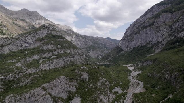 Drone video of frontal plane advancing on the Sh20 highway in Albania, at the height of Javor and Mreg, snake road, small houses of the town can be seen, cloudy sky