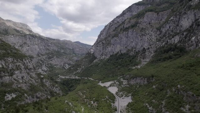 Drone video of frontal plane advancing on the Sh20 highway in Albania, at the height of Javor and Mreg, snake road, small houses of the town can be seen, cloudy sky