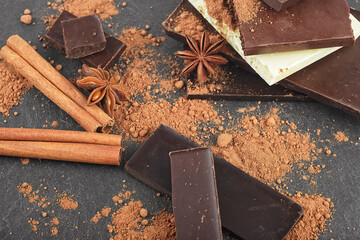 Broken chocolate pieces, cocoa powder, cinnamon sticks and anise stars on a black background