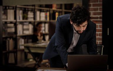 Obraz premium Caucasian successful professional diligent bearded and mustache male businessman in formal suit sitting at work desk typing laptop computer keyboard working late overtime in company office at night
