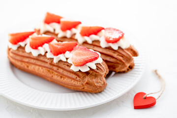 Eclairs with cream and strawberries on a white plate. Valentine's Day Concept