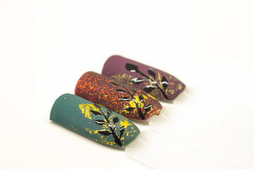 Autumnal nail designs on tips. Green, red and bordeaux matte gel polish, golden aluminium foil and black floral decor. Selective focus on the details, object isolated on white background.
