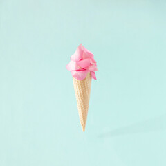 Ice cream cone with pink rose petals on blue background. Summer minimal concept. Flat lay.