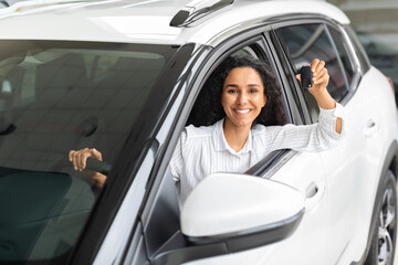Happy young woman sitting inside white car, showing key