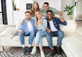 Emotional international group of friends sitting on couch at home, showing different gestures, smiling at camera