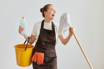 Portrait of happy funny woman wearing brown apron and jeans washing floor at home, posing with...