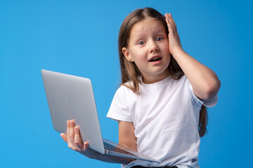Portrait of a little girl holding laptop computer while standing against blue background