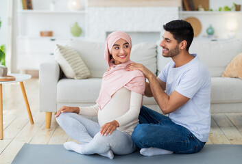Loving arab husband massaging his pregnant wife, woman feeling relaxed, spouses exercising together on mat
