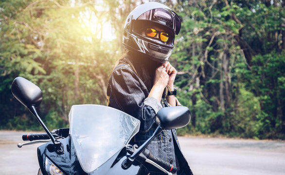 Confidence Asian woman wearing a motorcycle helmet before riding. Helmets contribute to motorcycle safety by protecting the rider's head. © boyloso