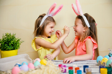 Two little girls in bunnies ears paint Easter eggs and pait each othes. Preparing for Easter 