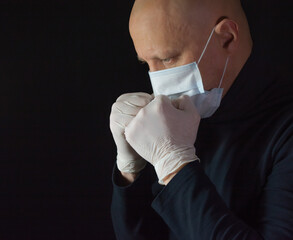Man in a medical mask, grief and emotions, black background. Concept: prayer and protection against...