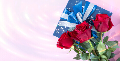 A gift box and a bouquet of red roses on a pink background with highlights of lights. The concept of greetings for Valentine's Day, anniversary, Mother's Day and birthday, copy space, top view.