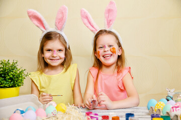 Two child girls in fun paint and decorate Easter eggs while wear bunny ears. Preparing for Easter