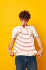 Young curly-haired man striped t shirt posing summer clothing yellow background unaltered