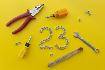 The number 23 of nuts with different tools on a yellow background. Defender of the Fatherland Day