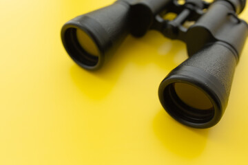 Binoculars on a light yellow background. Banner. Flat position, side view
